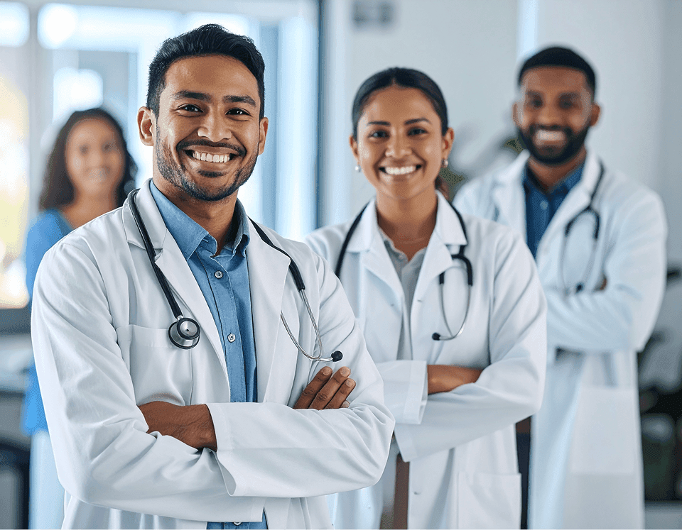 Fotografia de três profissionais de saúde sorrindo de braços cruzados, liderados por um médico com estetoscópio, representando uma equipe focada em um atendimento ao cidadão mais ágil e organizado na saúde pública.